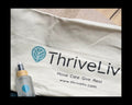 White mat bag with 'ThriveLiv' logo and a bottle of grip spray on a wooden surface.