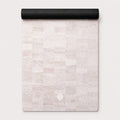 A rolled-up yoga mat with a light beige and off-white stone tile pattern, featuring the ThriveLiv logo at the bottom, set against a clean off-white background.