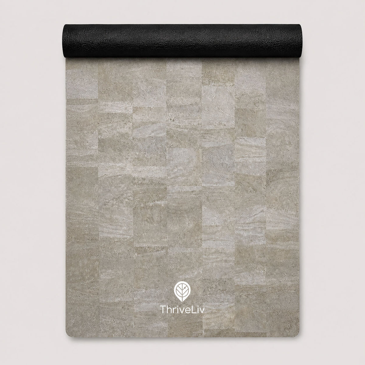 A rectangular yoga mat with a light gray stone tile pattern, partially unrolled to show its black textured underside, featuring the ThriveLiv logo at the bottom.