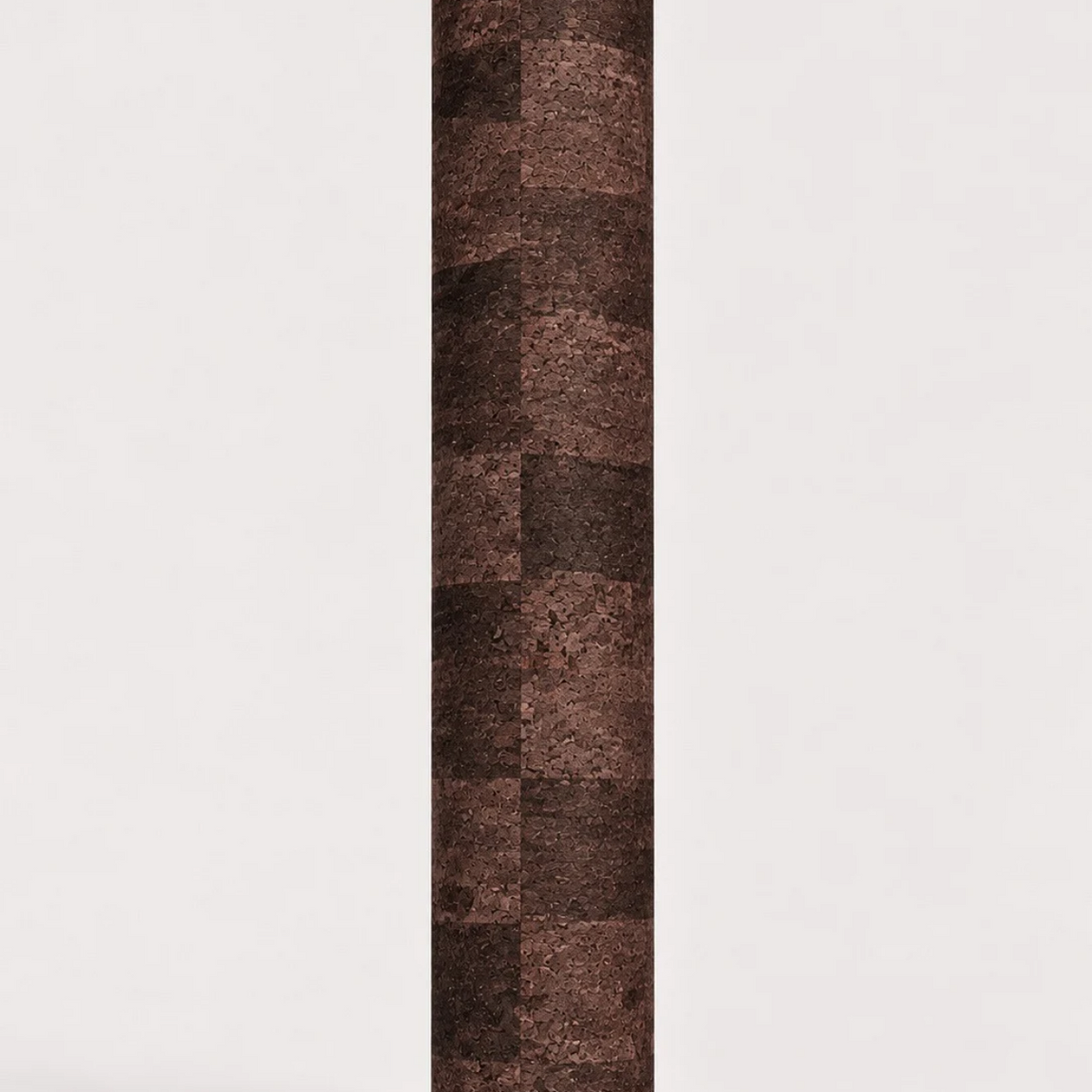A vertical yoga mat rolled up, featuring a textured patchwork pattern of dark brown and reddish-brown cork-like squares, centered on a plain white background.