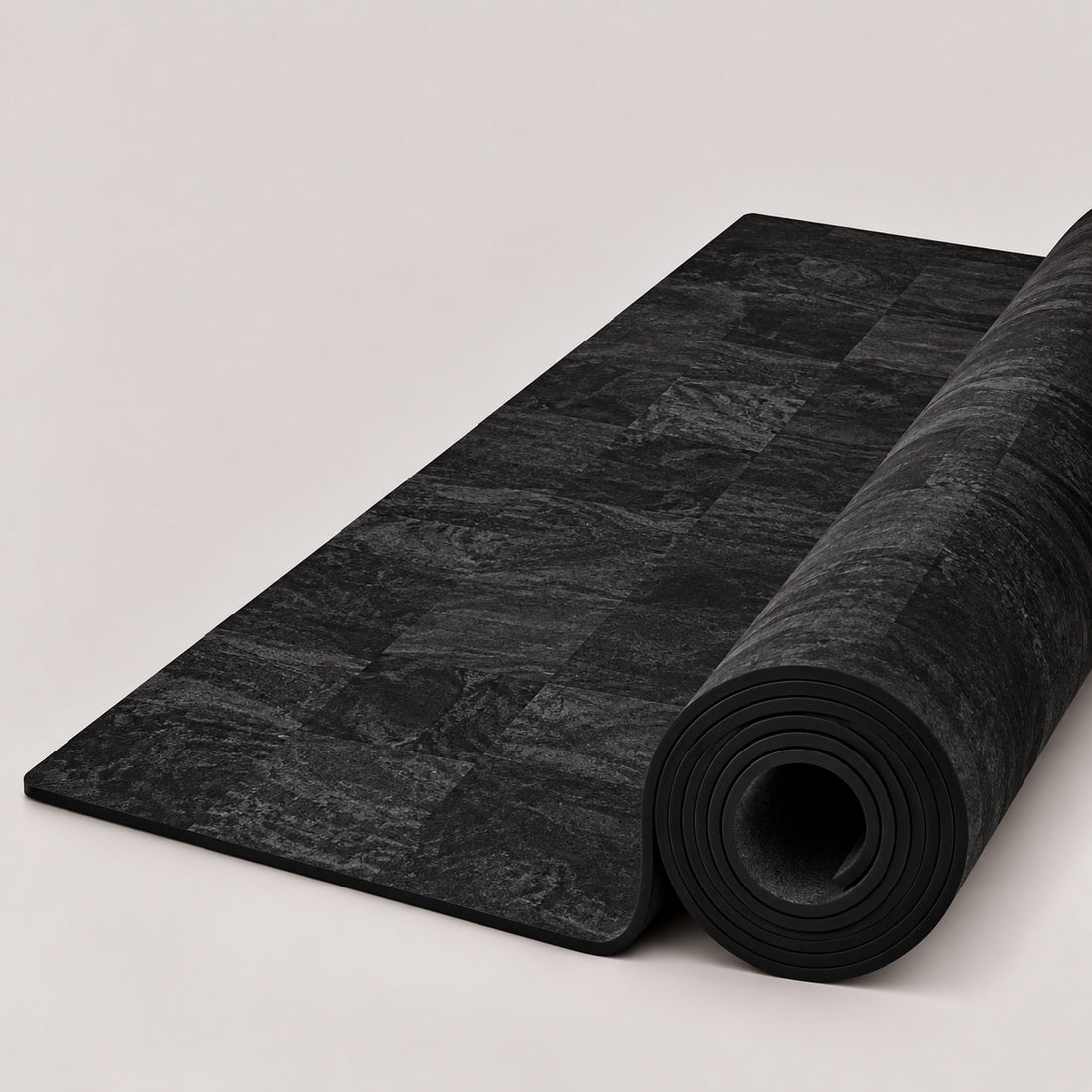 A black textured yoga mat with a subtle checkerboard pattern of dark charcoal squares, featuring the white ThriveLiv logo near the bottom, shown partially unrolled against a light off-white background.