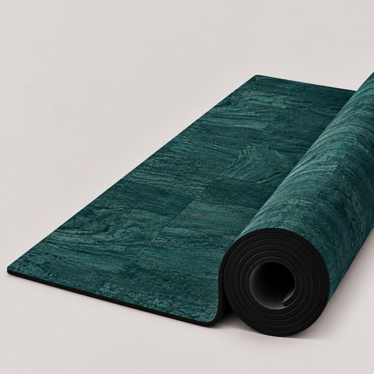 Grass tri-blend cork yoga mat in rich teal and deep green tones, partially rolled to reveal its black underside, photographed on a clean white studio background.
