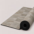 A rolled exercise or yoga mat with a gray stone-look textured top and a black underside, shown on a clean light beige background.