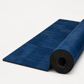 Water tri-blend cork yoga mat in rich deep blue tones, partially rolled to reveal its black underside, photographed on a clean white studio background.